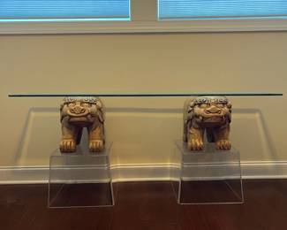 C42 - $450. Foo Dog Side Table. Glass top with lucite bases. Measures 66" x 15" deep x 28.5" tall. Dogs are porcelain material. 