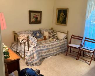 Vintage brass daybed with floral bedding and pillows—classic guest room charm, wooden folding chairs, art supplies, luggage for your next trip!