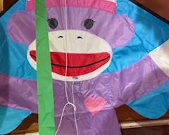 Cute purple sock-monkey kite with bright colors and fun details — great for kids, outdoor play, or adding whimsy to a backyard décor setup.