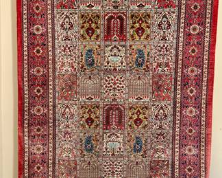 This is a finely woven Persian rug, likely from the mid-20th century, featuring a traditional medallion design within a rectangular field. The central area is divided into a grid of smaller panels, each showcasing intricate floral motifs, boteh (paisley) shapes, and possibly stylized trees or mihrabs (prayer niches). The color palette is dominated by deep reds, blues, greens, and creams, characteristic of dyes used in Persian rug making. The border consists of multiple bands, including a prominent floral pattern and narrower geometric designs. The rug is finished with a fringe.