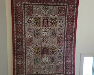 This is a finely woven Persian rug, likely from the mid-20th century, featuring a traditional medallion design within a rectangular field. The central area is divided into a grid of smaller panels, each showcasing intricate floral motifs, boteh (paisley) shapes, and possibly stylized trees or mihrabs (prayer niches). The color palette is dominated by deep reds, blues, greens, and creams, characteristic of dyes used in Persian rug making. The border consists of multiple bands, including a prominent floral pattern and narrower geometric designs. The rug is finished with a fringe.