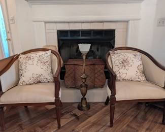 traditional wood-framed accent chairs with a curved back and beige fabric upholstery, throw pillow, wooden chest / box, tall brass lamp