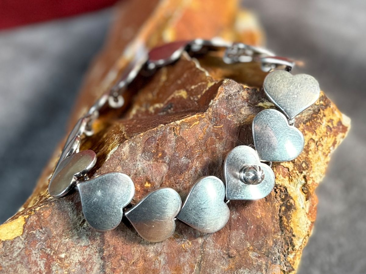 This lot features an iconic sterling silver hearts bracelet, a delightful classic design by Danish modernist Karl-Gustav Hansen for Hans Hansen, made in Denmark circa 1950s. Karl Gustav Hansen was the son Hans Hansen and later merged with the Georg Jensen company. This bracelet has the Hans Hansen designed screw-down clasp lock, measures 7” with a total approx. weight of 28.80 grams. Maker mark present as shown in photos.