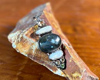 This lot features a stunning studio made pendant, crafted with sterling silver and features numerous stones including Citrine, Peridot, Biwa Pearl, & Labradorite. This pendant measures, 2.5” H and has a total approx. weight of 15.65 grams.