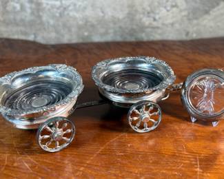 This lot features an antique Victorian silver plated wine coaster trolley made in Japan along with a sterling silver wine coaster by Frank Whiting & Co.