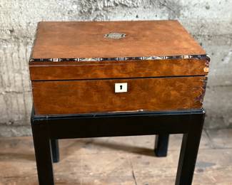 This lot features a 19th century burled walnut writing slope on a lacquered stand. The burled walnut top has a central brass inlaid presentation plaque that is inscribed. This piece measures (on stand), 18” H x 15.5” H x 11” D.