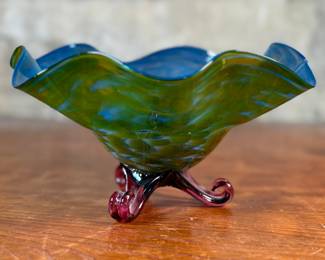 This lot features a stunning studio made footed glass bowl by listed artist, Mark Woodham. Signed and dated underneath and was made during Woodham’s time creating works at the One Eared Cow Glass Studio. This bowl measures, 5” H x 9” W x 9” D and is in excellent condition.