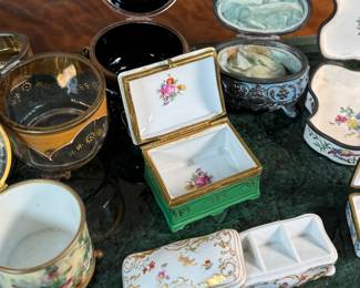 This lot features a large collection of antique trinket boxes that are primarily porcelain. Many of them contain maker marks and are held on a vintage green tray that is included.