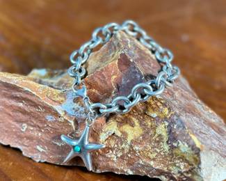 This lot features a sterling silver starfish charm bracelet with an inlay stone by designer, Elsa Peretti for Tiffany & Co. This bracelet measures 7” and has a total approx. weight of 34.32 grams.