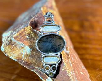 This lot features a stunning studio made pendant, crafted with sterling silver and features numerous stones including Citrine, Peridot, Biwa Pearl, & Labradorite. This pendant measures, 2.5” H and has a total approx. weight of 15.65 grams.