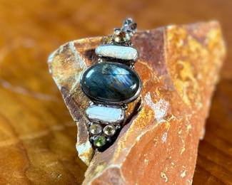 This lot features a stunning studio made pendant, crafted with sterling silver and features numerous stones including Citrine, Peridot, Biwa Pearl, & Labradorite. This pendant measures, 2.5” H and has a total approx. weight of 15.65 grams.