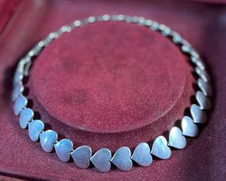 This lot features an iconic sterling silver heart necklace titled, "Chain of Hearts". A Hans Hansen design for Georg Jensen with a total approx. weight of 61.77 grams and measures, 15.5”. Comes in the original box and in excellent condition. The design features a series of meticulously crafted, solid silver heart shapes linked together to create an articulated, choker-style necklace. Maker marks present as shown in photos.