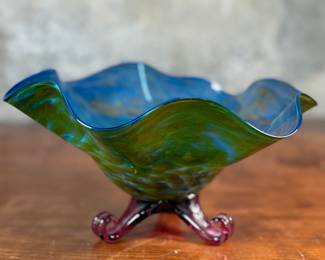 This lot features a stunning studio made footed glass bowl by listed artist, Mark Woodham. Signed and dated underneath and was made during Woodham’s time creating works at the One Eared Cow Glass Studio. This bowl measures, 5” H x 9” W x 9” D and is in excellent condition.