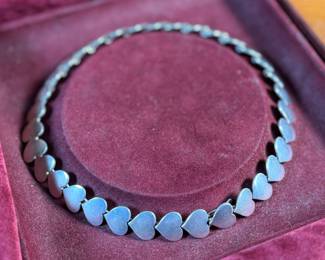 This lot features an iconic sterling silver heart necklace titled, "Chain of Hearts". A Hans Hansen design for Georg Jensen with a total approx. weight of 61.77 grams and measures, 15.5”. Comes in the original box and in excellent condition. The design features a series of meticulously crafted, solid silver heart shapes linked together to create an articulated, choker-style necklace. Maker marks present as shown in photos.