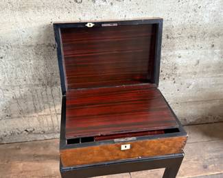 This lot features a 19th century burled walnut writing slope on a lacquered stand. The burled walnut top has a central brass inlaid presentation plaque that is inscribed. This piece measures (on stand), 18” H x 15.5” H x 11” D.