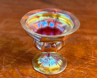 This lot features an iridescent gold Tiffany Favrile sherbet glass with maker marks present underneath as shown in photos. One small repair on the foot ring and measures, 3.5” H x 4” W x 4” D.
