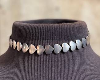 This lot features an iconic sterling silver heart necklace titled, "Chain of Hearts". A Hans Hansen design for Georg Jensen with a total approx. weight of 61.77 grams and measures, 15.5”. Comes in the original box and in excellent condition. The design features a series of meticulously crafted, solid silver heart shapes linked together to create an articulated, choker-style necklace. Maker marks present as shown in photos.