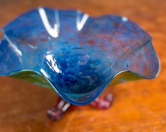 This lot features a stunning studio made footed glass bowl by listed artist, Mark Woodham. Signed and dated underneath and was made during Woodham’s time creating works at the One Eared Cow Glass Studio. This bowl measures, 5” H x 9” W x 9” D and is in excellent condition.