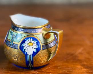 This lot features an antique sugar bowl with lid and a cream pitcher set, hand-painted in an Art Nouveau style by an artist named Osborne for Pickard China. The set features a design with stylized flowers on a cobalt ground and multiple borders of blue and white luster colors.