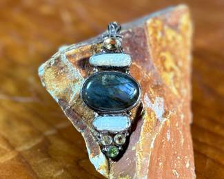 This lot features a stunning studio made pendant, crafted with sterling silver and features numerous stones including Citrine, Peridot, Biwa Pearl, & Labradorite. This pendant measures, 2.5” H and has a total approx. weight of 15.65 grams.