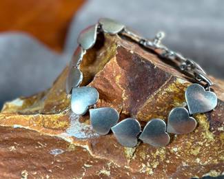This lot features an iconic sterling silver hearts bracelet, a delightful classic design by Danish modernist Karl-Gustav Hansen for Hans Hansen, made in Denmark circa 1950s. Karl Gustav Hansen was the son Hans Hansen and later merged with the Georg Jensen company. This bracelet has the Hans Hansen designed screw-down clasp lock, measures 7” with a total approx. weight of 28.80 grams. Maker mark present as shown in photos.