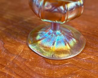 This lot features an iridescent gold Tiffany Favrile sherbet glass with maker marks present underneath as shown in photos. One small repair on the foot ring and measures, 3.5” H x 4” W x 4” D.