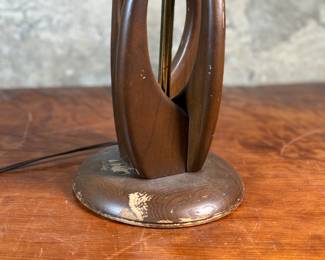 This lot features a mid-century modern sculptural table lamp, made of walnut and brass. Minor wear throughout as shown in photos and light turns on periodically (will need to some servicing or love). This lamp measures, 38” H x 7” W x 7” D.