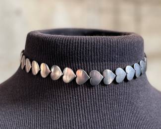 This lot features an iconic sterling silver heart necklace titled, "Chain of Hearts". A Hans Hansen design for Georg Jensen with a total approx. weight of 61.77 grams and measures, 15.5”. Comes in the original box and in excellent condition. The design features a series of meticulously crafted, solid silver heart shapes linked together to create an articulated, choker-style necklace. Maker marks present as shown in photos.