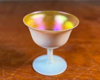 This lot features a Steuben Gold Aurene Calcite sherbet glass. This type of art glass was developed by Frederick Carder at the Steuben Glass Works in the early 1900s. This glass measures, 4” H x 4” W x 4” D and is in very good condition.