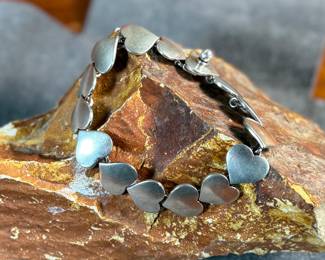 This lot features an iconic sterling silver hearts bracelet, a delightful classic design by Danish modernist Karl-Gustav Hansen for Hans Hansen, made in Denmark circa 1950s. Karl Gustav Hansen was the son Hans Hansen and later merged with the Georg Jensen company. This bracelet has the Hans Hansen designed screw-down clasp lock, measures 7” with a total approx. weight of 28.80 grams. Maker mark present as shown in photos.