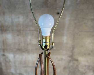 This lot features a mid-century modern sculptural table lamp, made of walnut and brass. Minor wear throughout as shown in photos and light turns on periodically (will need to some servicing or love). This lamp measures, 38” H x 7” W x 7” D.