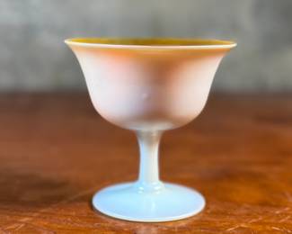 This lot features a Steuben Gold Aurene Calcite sherbet glass. This type of art glass was developed by Frederick Carder at the Steuben Glass Works in the early 1900s. This glass measures, 4” H x 4” W x 4” D and is in very good condition.