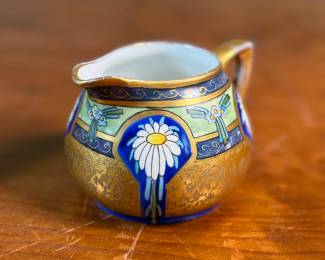 This lot features an antique sugar bowl with lid and a cream pitcher set, hand-painted in an Art Nouveau style by an artist named Osborne for Pickard China. The set features a design with stylized flowers on a cobalt ground and multiple borders of blue and white luster colors.