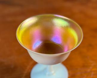 This lot features a Steuben Gold Aurene Calcite sherbet glass. This type of art glass was developed by Frederick Carder at the Steuben Glass Works in the early 1900s. This glass measures, 4” H x 4” W x 4” D and is in very good condition.