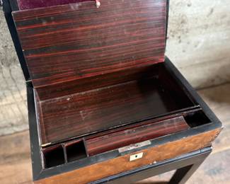 This lot features a 19th century burled walnut writing slope on a lacquered stand. The burled walnut top has a central brass inlaid presentation plaque that is inscribed. This piece measures (on stand), 18” H x 15.5” H x 11” D.