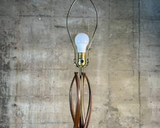 This lot features a mid-century modern sculptural table lamp, made of walnut and brass. Minor wear throughout as shown in photos and light turns on periodically (will need to some servicing or love). This lamp measures, 38” H x 7” W x 7” D.