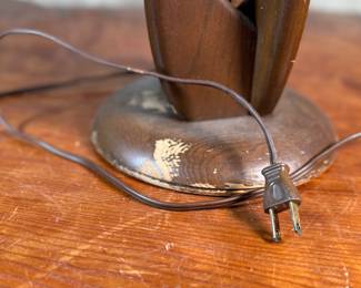 This lot features a mid-century modern sculptural table lamp, made of walnut and brass. Minor wear throughout as shown in photos and light turns on periodically (will need to some servicing or love). This lamp measures, 38” H x 7” W x 7” D.