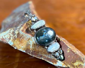 This lot features a stunning studio made pendant, crafted with sterling silver and features numerous stones including Citrine, Peridot, Biwa Pearl, & Labradorite. This pendant measures, 2.5” H and has a total approx. weight of 15.65 grams.