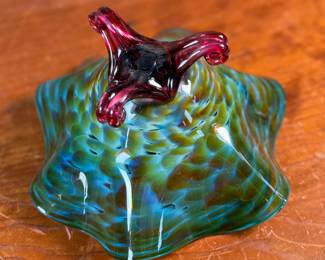 This lot features a stunning studio made footed glass bowl by listed artist, Mark Woodham. Signed and dated underneath and was made during Woodham’s time creating works at the One Eared Cow Glass Studio. This bowl measures, 5” H x 9” W x 9” D and is in excellent condition.