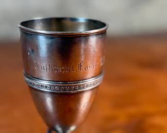This lot features a 1873 birth commemorative sterling silver footed cup retailed by Ohio jeweler & silversmith, William Wilson McGrew (1833-1893). This silver cup was made to commemorate the birth of Nathaniel Foster Wilshire, son of George Wilshire who was a railroad and business tycoon. This cup measures, 5.25” H x 2.75” W x 4” D with a total approx. weight of 176.61 grams. Maker marks present underneath as shown in photos.