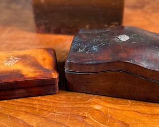 This lot features a collection of boxes from the 19th and 20th century. The two smaller ones up top are crafted from leather, the two below from wood, and the one in front is metal.