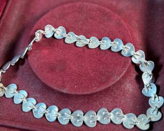 This lot features an iconic sterling silver heart necklace titled, "Chain of Hearts". A Hans Hansen design for Georg Jensen with a total approx. weight of 61.77 grams and measures, 15.5”. Comes in the original box and in excellent condition. The design features a series of meticulously crafted, solid silver heart shapes linked together to create an articulated, choker-style necklace. Maker marks present as shown in photos.