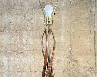 This lot features a mid-century modern sculptural table lamp, made of walnut and brass. Minor wear throughout as shown in photos and light turns on periodically (will need to some servicing or love). This lamp measures, 38” H x 7” W x 7” D.