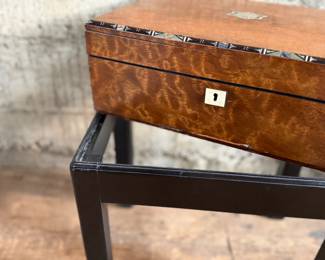 This lot features a 19th century burled walnut writing slope on a lacquered stand. The burled walnut top has a central brass inlaid presentation plaque that is inscribed. This piece measures (on stand), 18” H x 15.5” H x 11” D.