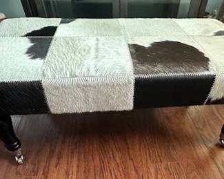 Rectangular patchwork cowhide ottoman or bench with turned wooden legs and casters.