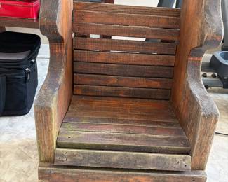 This is a rustic wooden armchair, possibly antique or handmade, featuring a slatted seat and backrest. 
