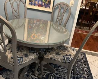 Gray sturdy round kitchen table with four chairs. Custom blue and gray upholstered seats.. heavy glass top.