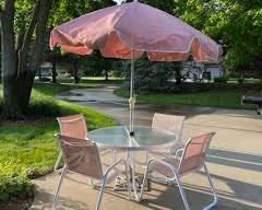 Round metal and glass patio table with central umbrella and 4 matching chairs.