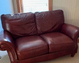 This is a burgundy leather loveseat with rolled arms and nailhead trim