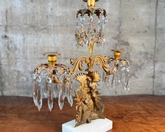 This lot features an antique, mid-19th century Victorian brass triple-light girandole candelabra with crystal prisms and a white marble base. This candelabra measures, 18” H x 15” W x 4” D. 
